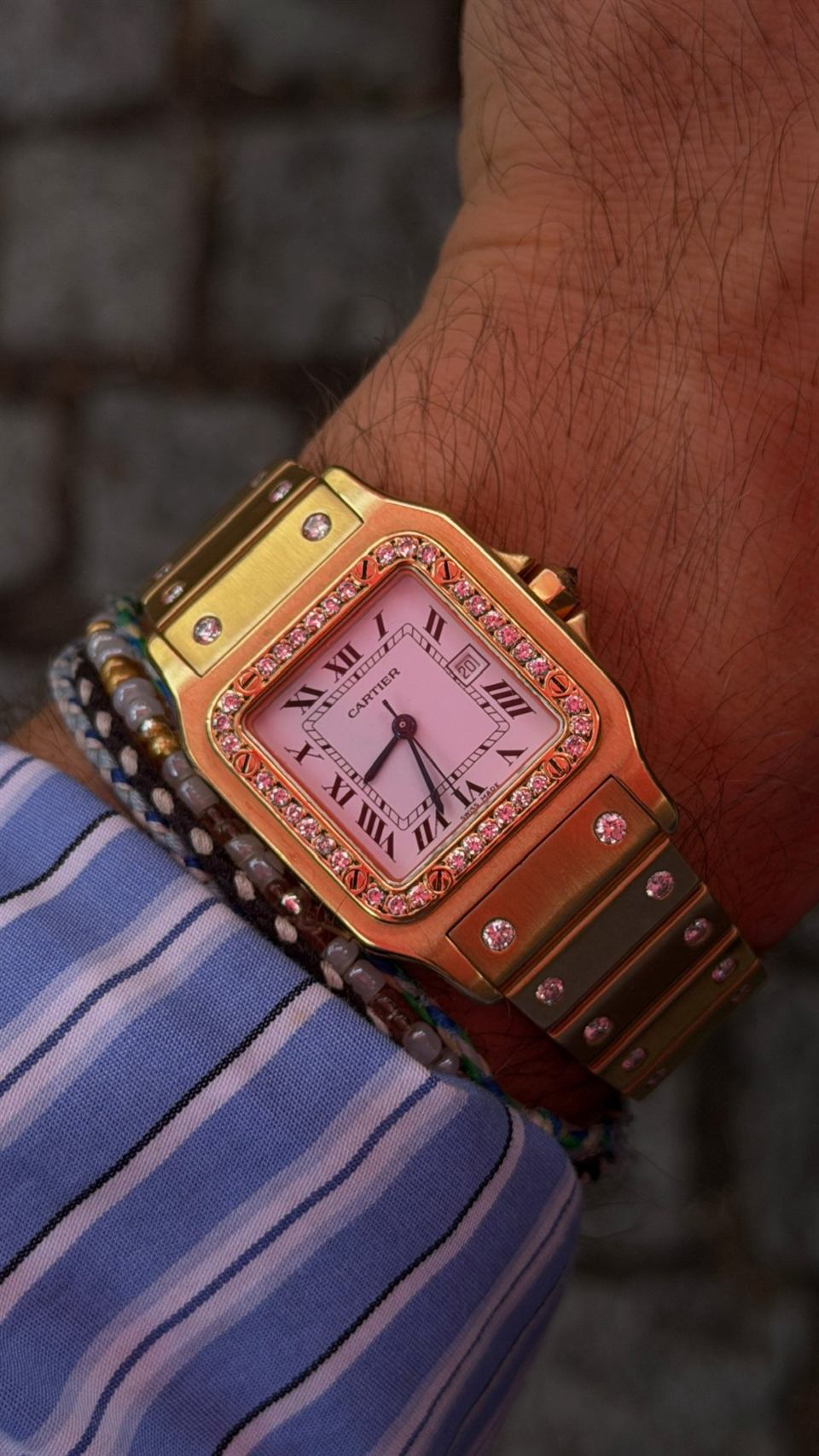 Cartier Santos in Gold mit rosafarbenem Zifferblatt und Diamantlünette am Handgelenk.