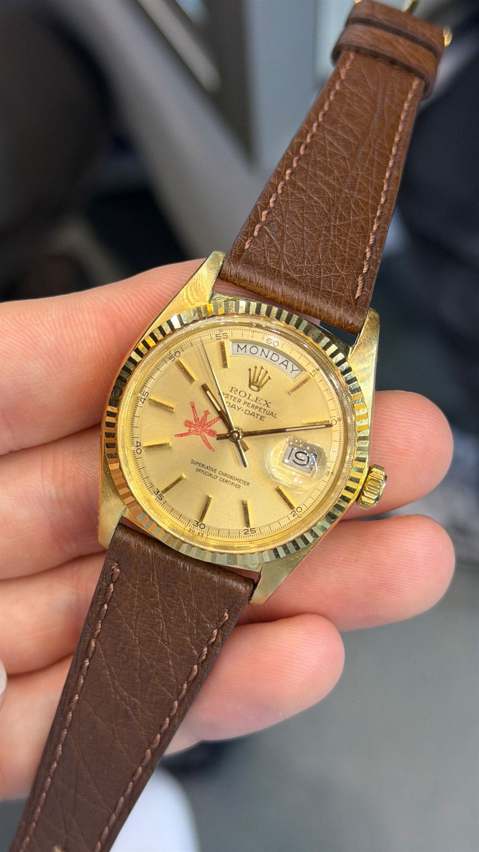 Rolex Day-Date in Gelbgold mit Emblem auf dem Zifferblatt, in der Hand gehalten.