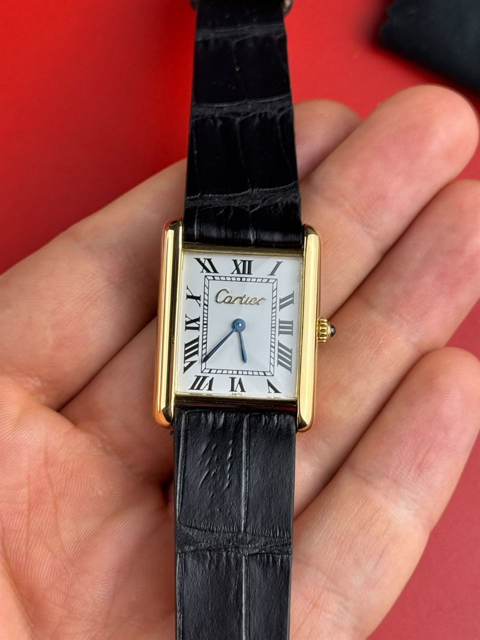 Cartier Tank mit schwarzem Lederband in einer offenen Hand.