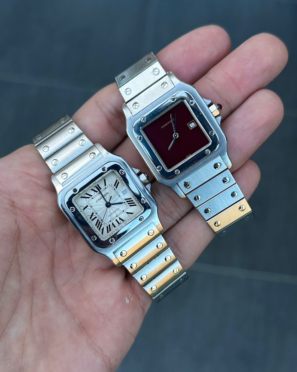 Zwei Cartier Santos in der offenen Hand, eine in Stahl mit weißem Zifferblatt, eine in Stahl und Gold mit rotem Zifferblatt