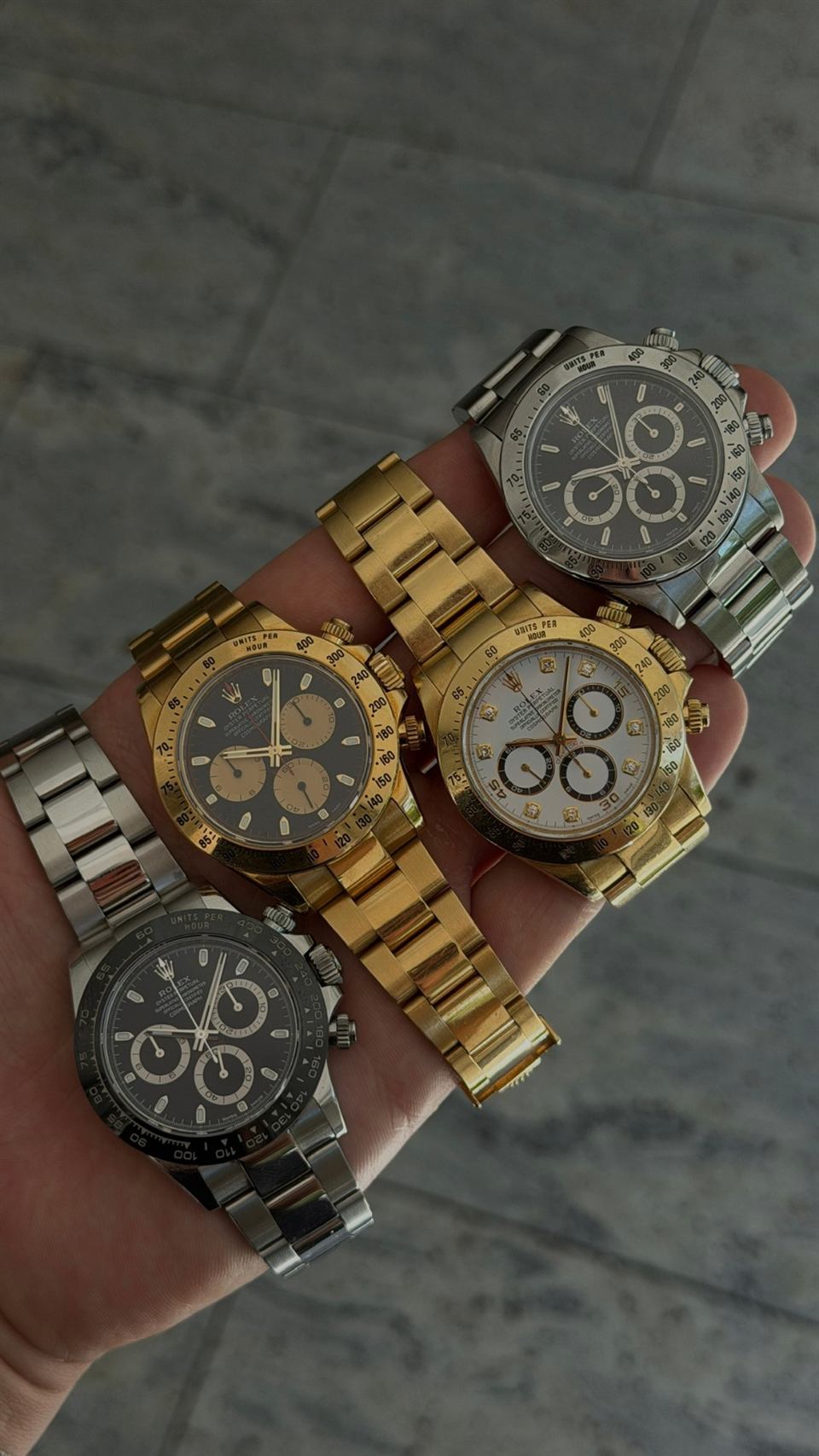 Vier Rolex Daytona in Stahl, Gold sowie Stahl und Gold, in einer Hand gehalten.