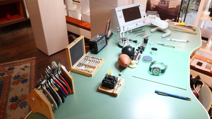 Werkbank eines Uhrmachers mit Pinzetten, Zeitwaage und einer Uhr auf grüner Unterlage.